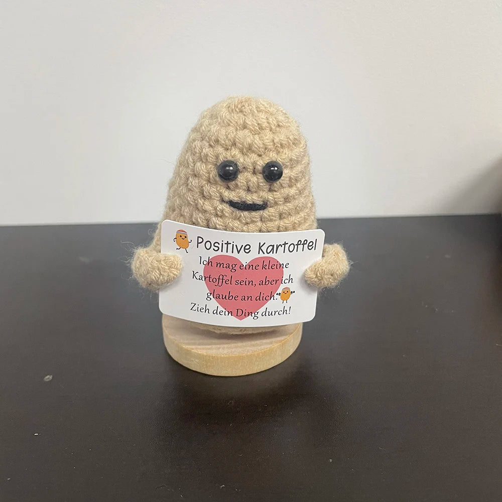 Handmade crochet potato plush doll holding a German sign that says "Ich mag eine kleine Kartoffel sein, aber ich glaube an dich. Zieh dein Ding durch!" meaning "I may be a tiny potato, but I believe in you. Go do your thing!